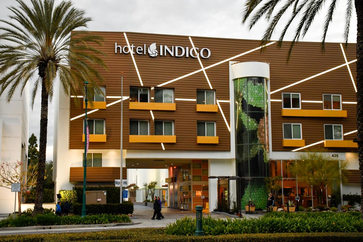 A palm tree next to the brown and orange façade of the Hotel Indigo Anaheim