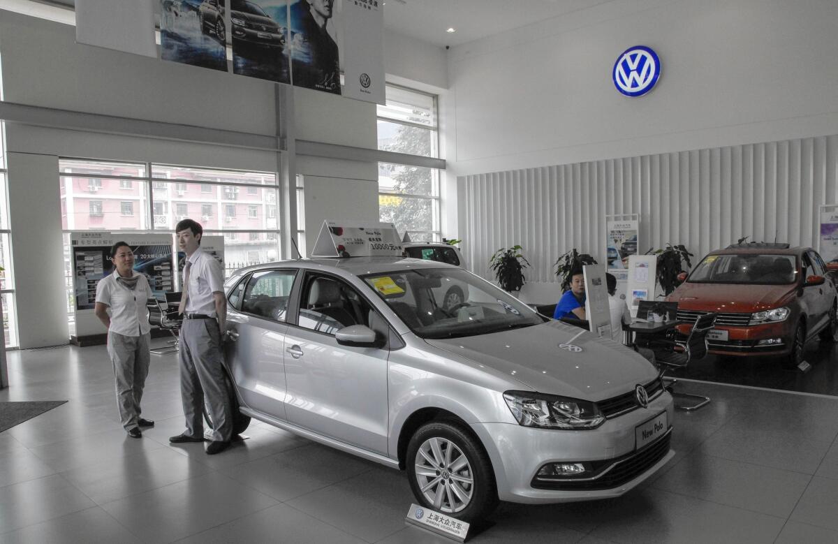 Sales staff wait for customers beside a vehicle model at a Shanghai Volkswagen dealership in Beijing on Aug. 5.