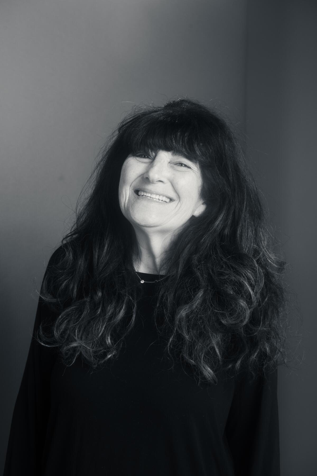 A vertical portrait of Ruth Reichl, photographed smiling and in black and white