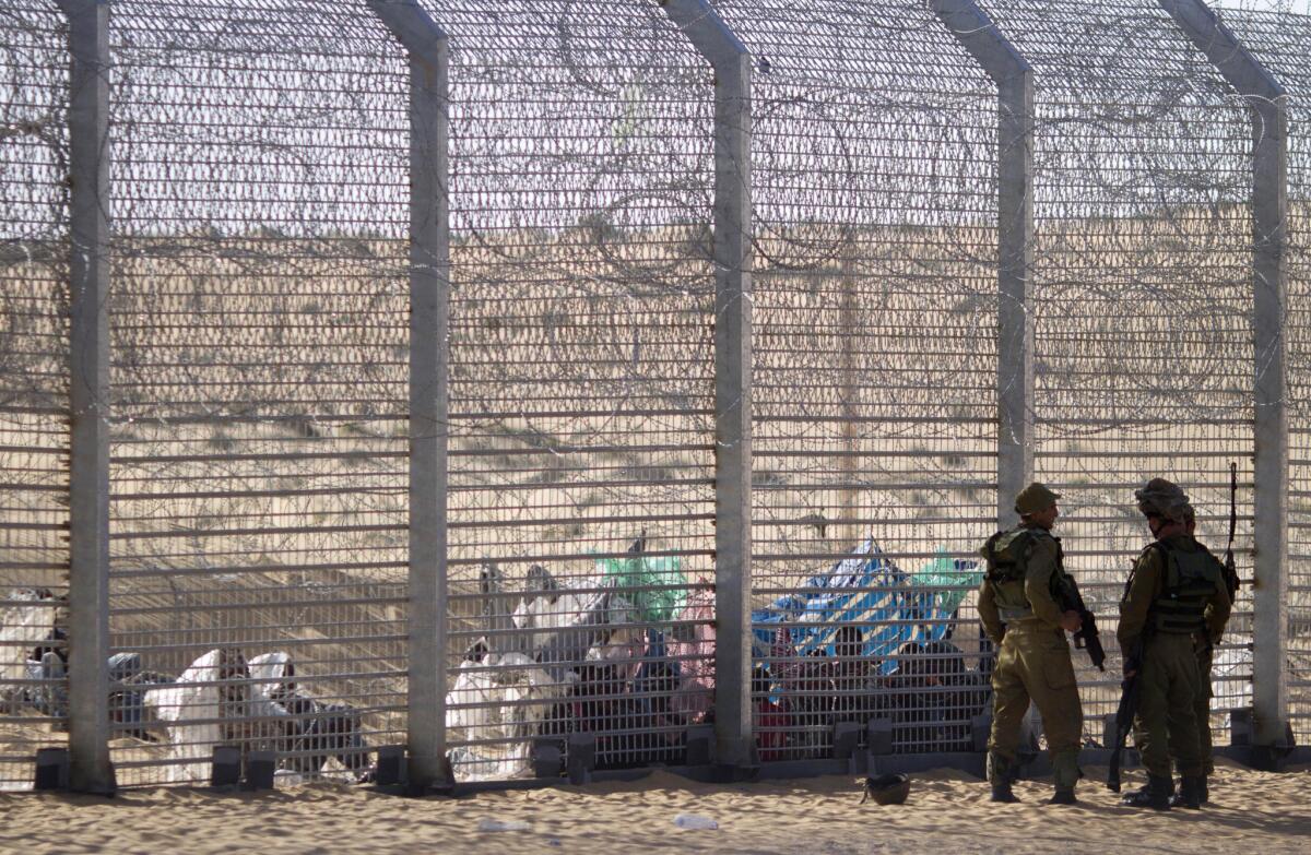 African refugees sit behind a border fence after attempting to cross from Egypt into Israel as Israeli soldiers stand guard nearby.