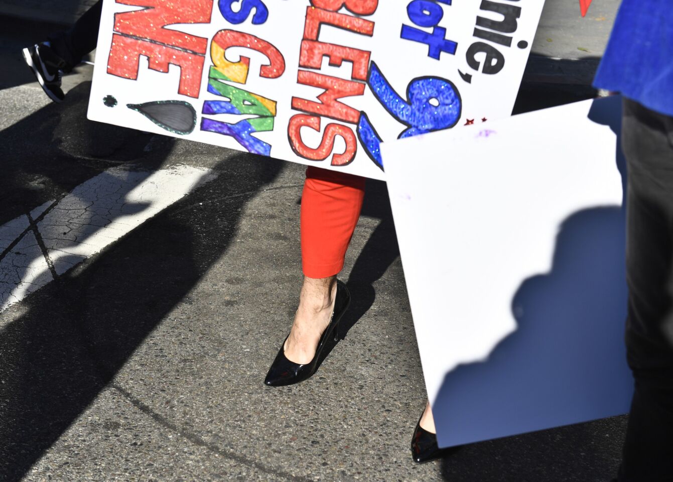 An orange suit and high heels worn by Ryan Tymensky peek out from under a handmade sign before the start of the women's march.
