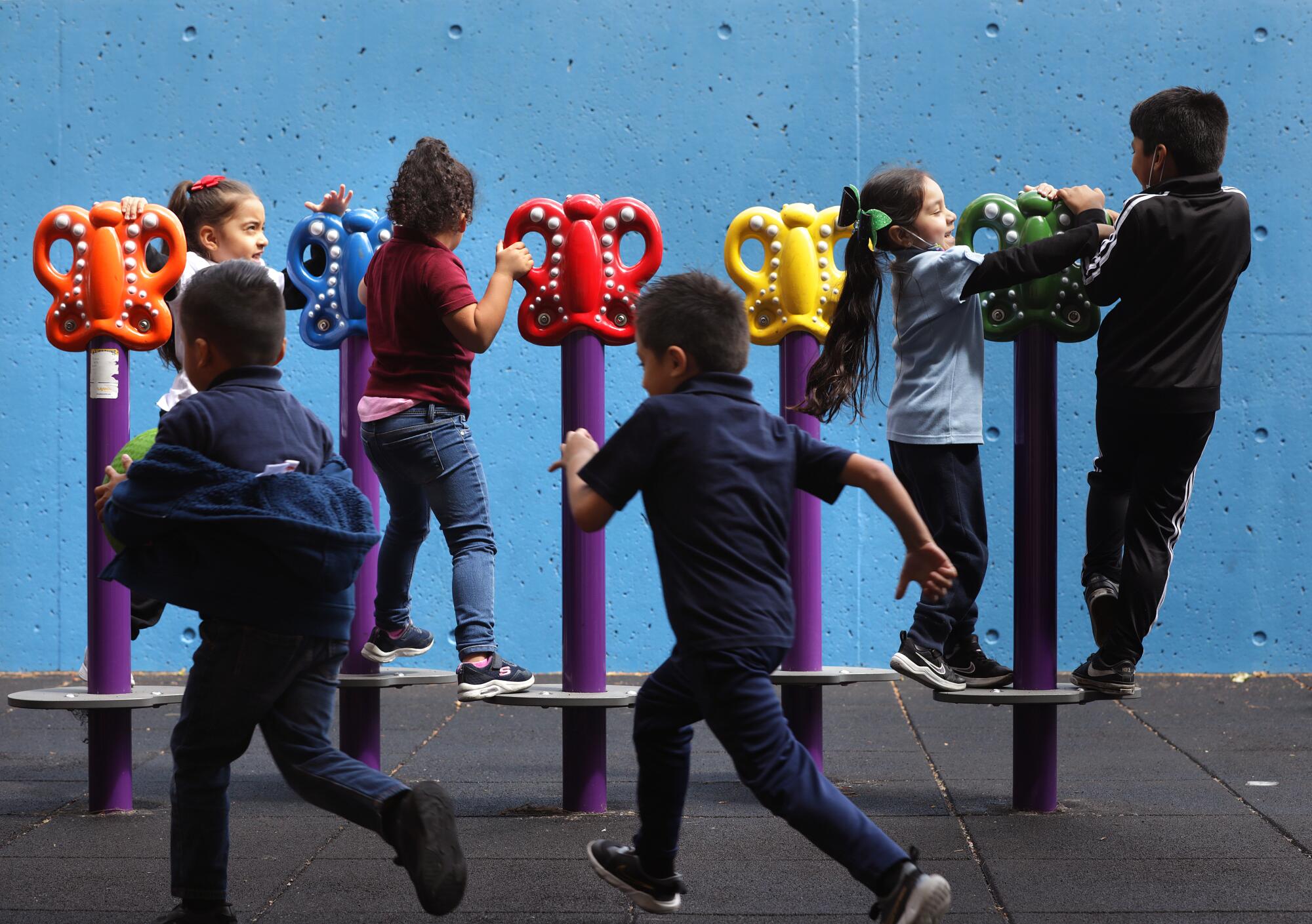 Small children stand on playground equipment as others rush to join them.