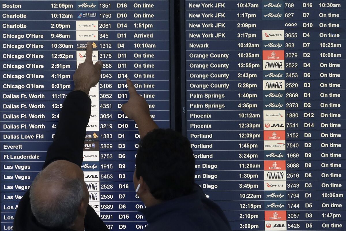 FILE - Two men point toward plane arrivals on a flight information board at San Francisco International Airport in San Francisco, Tuesday, Nov. 26, 2019. Forecasters say, Friday, March 11, 2022, a powerful, late-winter storm combining rivers of moisture and frigid temperatures is expected to dump snow from the Deep South all the way north to the Canadian border over the weekend that could cause travel problems and power outages across a wide part of the Eastern United States from late Friday through early next week. (AP Photo/Jeff Chiu)