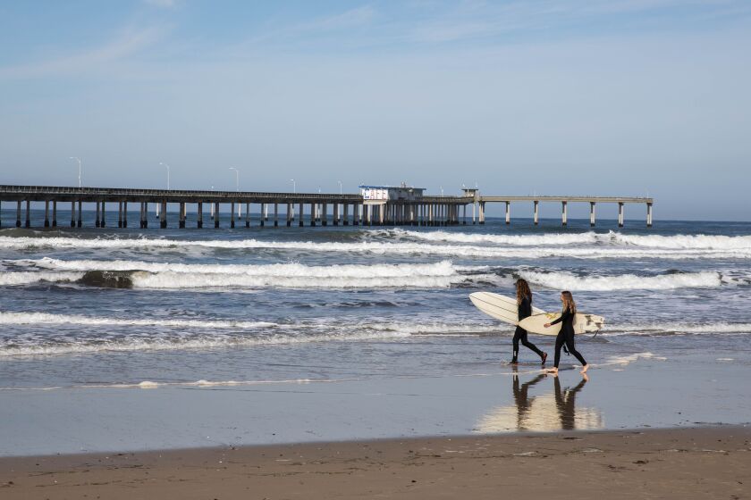 Surfers pass by Ocean Beach Pier at Ocean Beach in San Diego, CA on Monday March 27, 2023. The city of San Diego is moving forward with plans to repair or potential replace the pier in coming year sand will soon host a series of community workshops to gather input from the public. (Adriana Heldiz / The San Diego Union-Tribune)