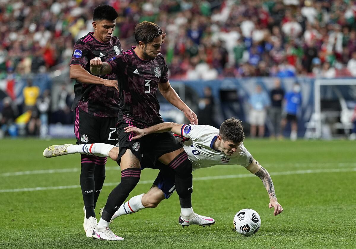 The United States' Christian Pulisic (10) is knocked down by Mexico's Jesús Gallardo (23) and Carlos Salcedo (3).