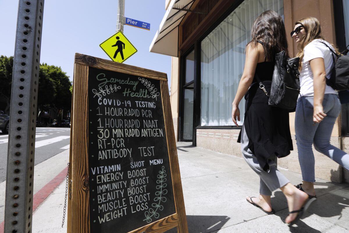 Two people walking past a sandwich board sign on a sidewalk