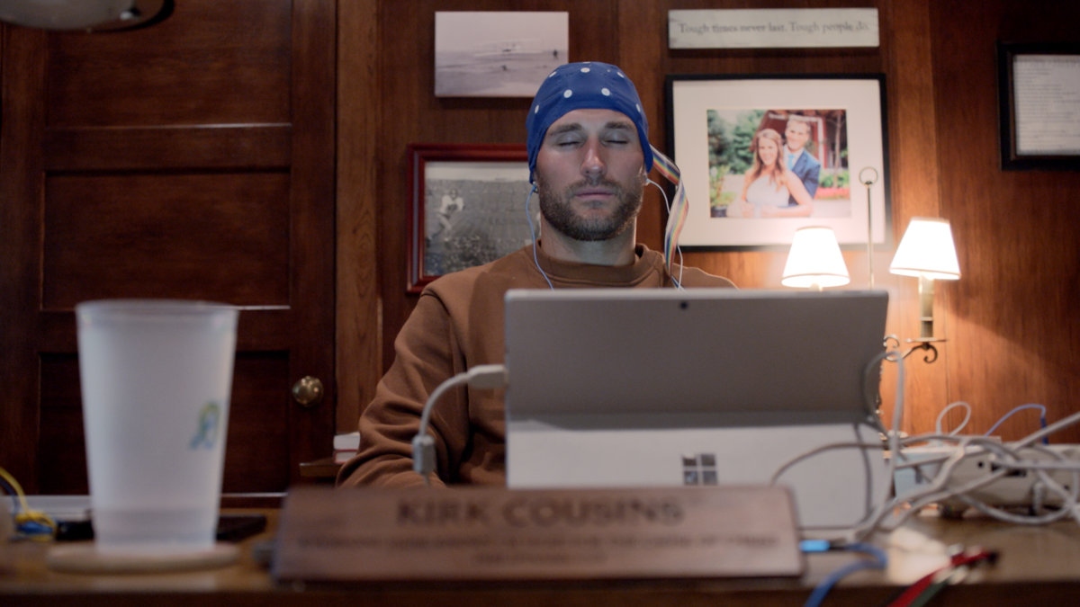 Quarterback Kirk Cousins sitting at a desk with a laptop with his eyes closed