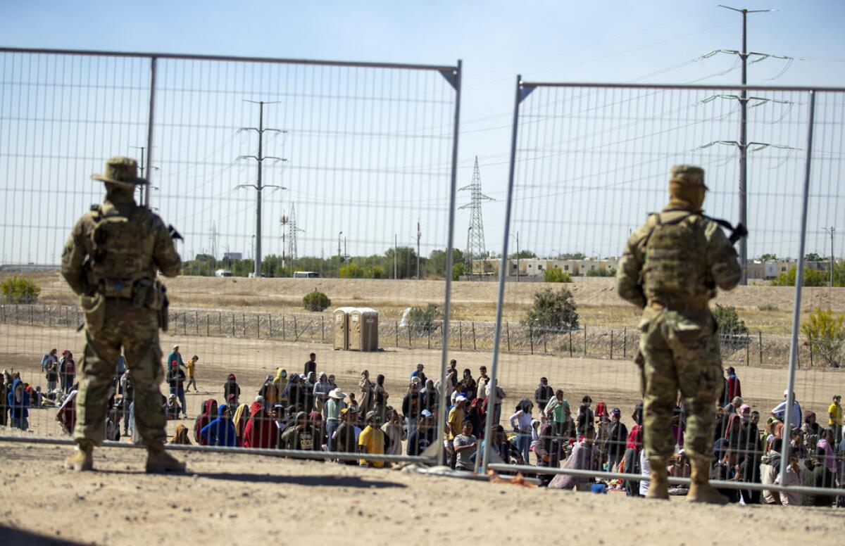 Migrantes esperan junto a una valla fronteriza 
