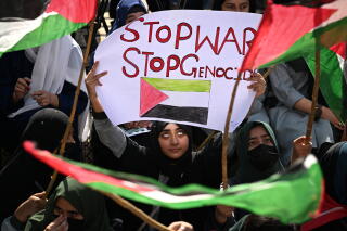 Women in head coverings wave green, white, black and red flags and a sign that says Stop War, Stop Genocide