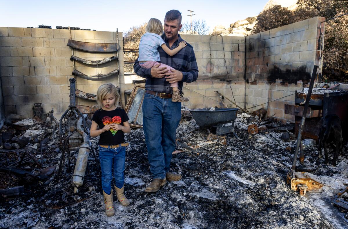 A man holds a small child as a girl stands with him in the ashes of a gutted building.