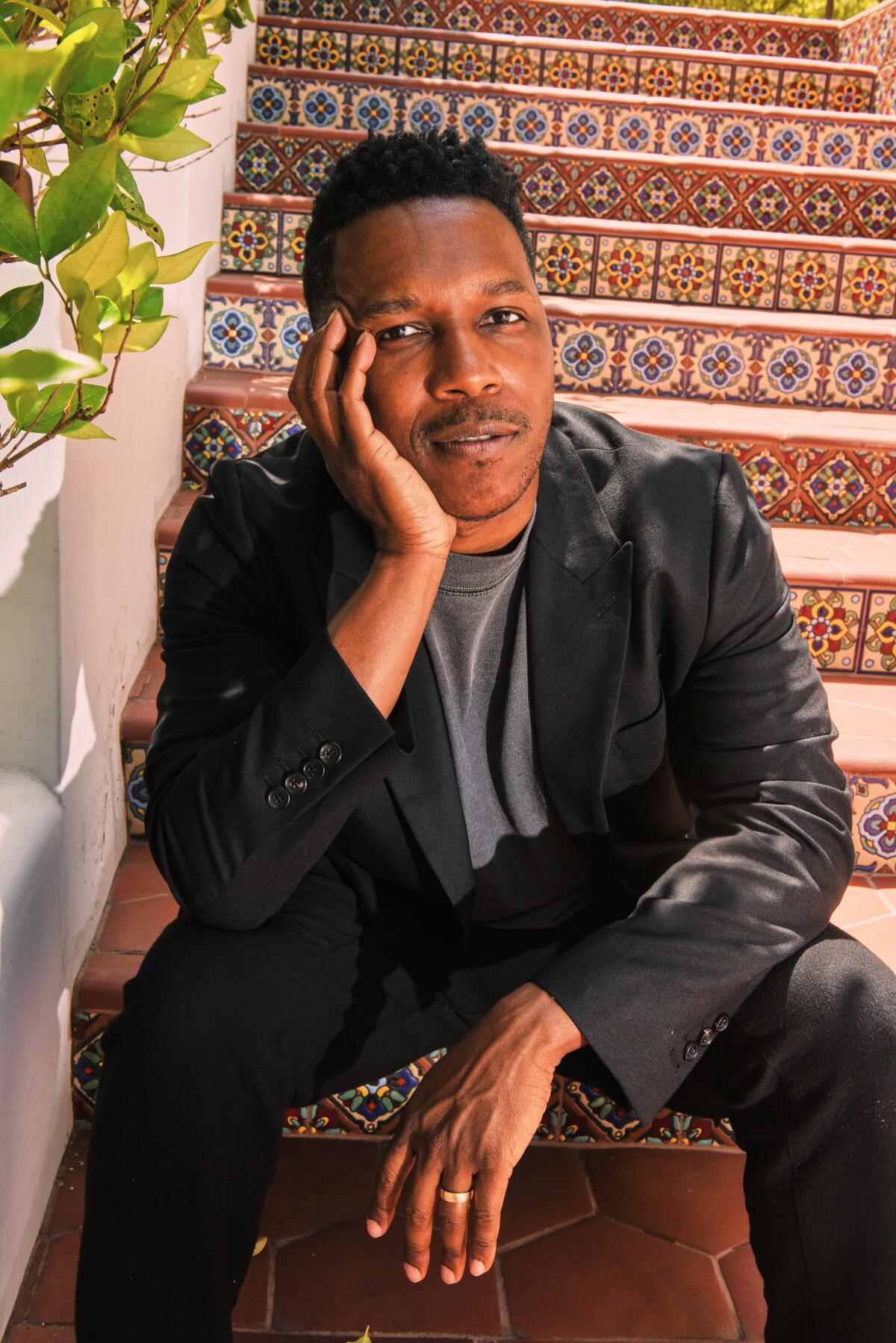 Leslie Odom Jr. sits on tiled steps with his chin on his hand.