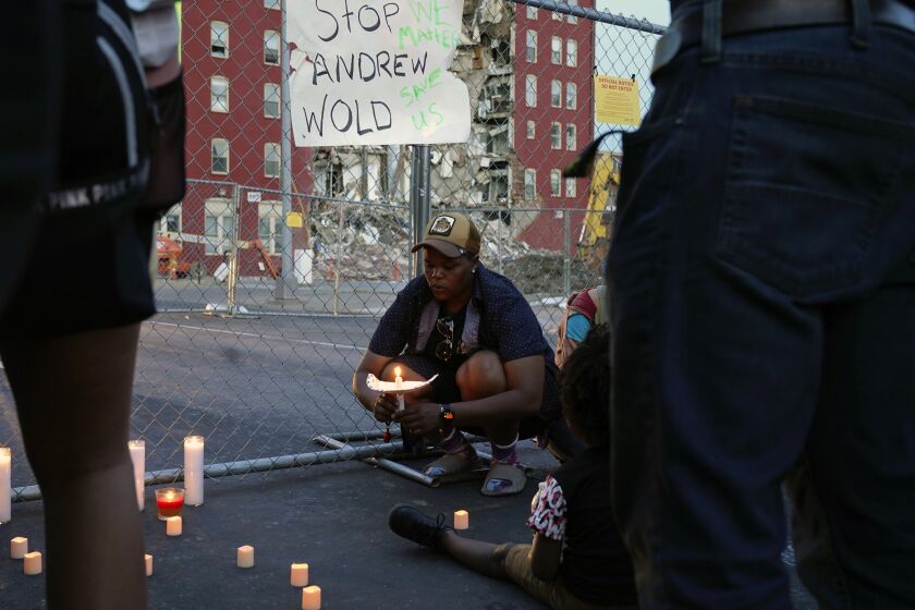 After asking a group of about 50 people gathered for a vigil to remain silent for five minutes in honor of the five people still unaccounted for, Raquel Sipp kneels with a candle at the scene of where an apartment building partially collapsed two days earlier, in Davenport, Iowa, Tuesday, May 30, 2023. Five residents of the six-story apartment building remained unaccounted for and authorities feared at least two of them might be stuck inside rubble that was too dangerous to search. (AP Photo/Erin Hooley)
