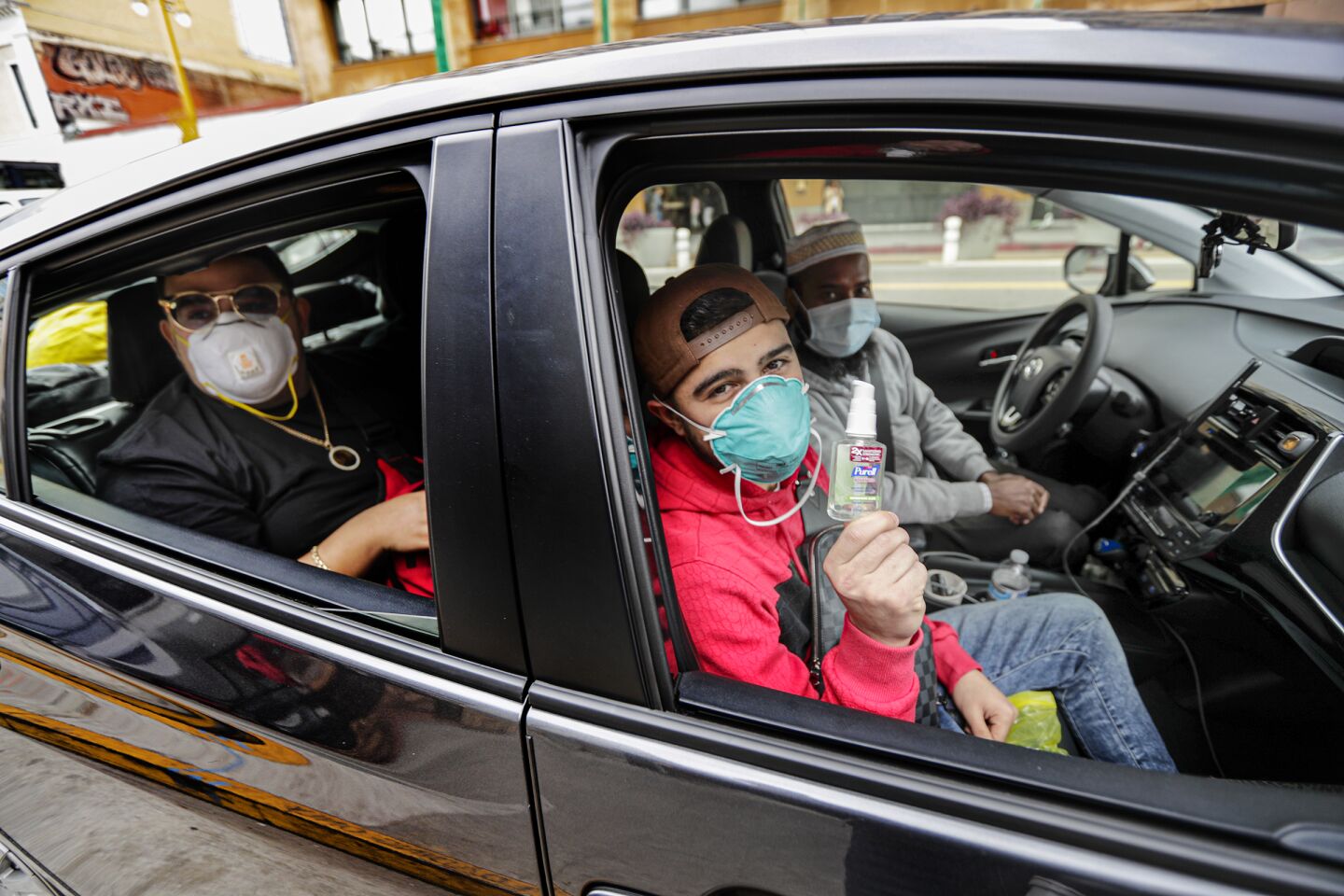Muhammad Faruq, an Uber driver, picks his ride Sotero Reyes, left, and Cristian Eguia, visitors from Houston, all in protective masks, from downtown Los Angeles.