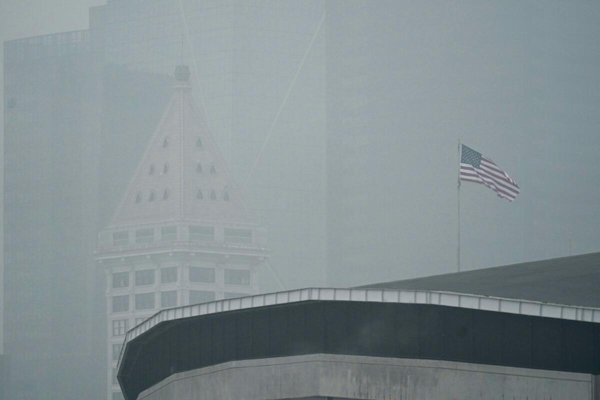 FILE - In this Sept. 14, 2020, file photo, a U.S. flag flies near Smith Tower in downtown Seattle as air thick with smoke from wildfires as seen over CenturyLink Field in Seattle. The damage caused by wildfires can be devastating, yet researchers say the smoke from the annually recurring blazes also delivers economic damage to areas that were never touched by the flames. (AP Photo/Ted S. Warren, File)