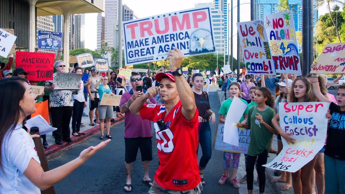 Edward Odquina, center, holds a "Make America Great Again" as he confronts anti-Trump protesters Friday in Honolulu.