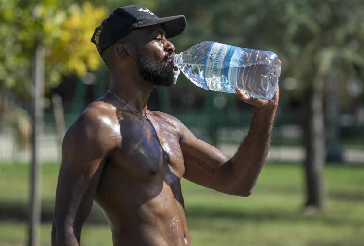 A shirtless man drinking from a large water bottle outdoors