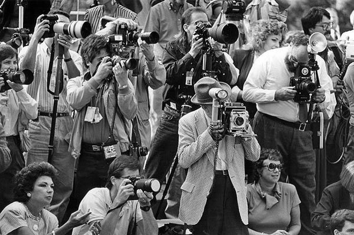 Clem Inspeak, in hat, holding a 40-year-old Crown Graphic 4 x 5 camera, is surrounded by modern equipment as he photographs the announcement of the members of the Tournament of Roses court.