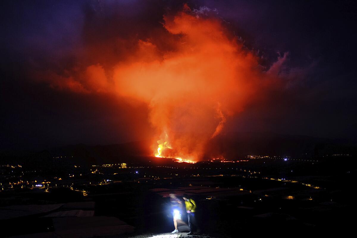 Dos personas caminan durante la noche mientras un volcán expulsa lava, en La Palma, Islas Canarias, 