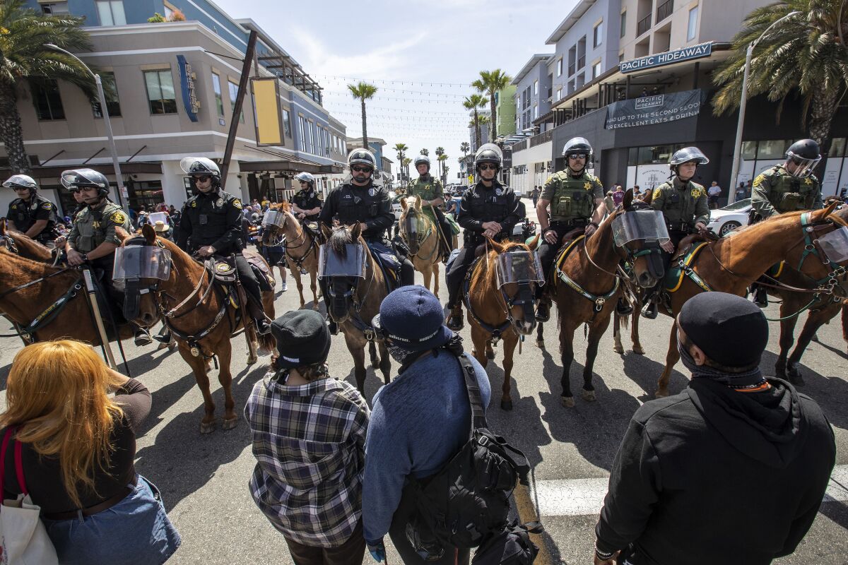 Protesters face a group of mounted police officers Sunday in Huntington Beach