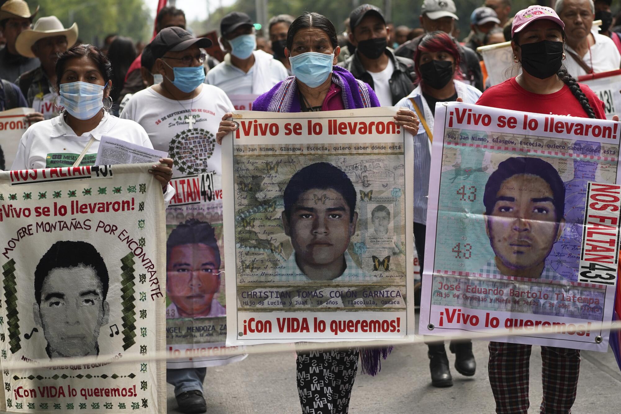 People wearing masks march while holding signs with images of individual men.