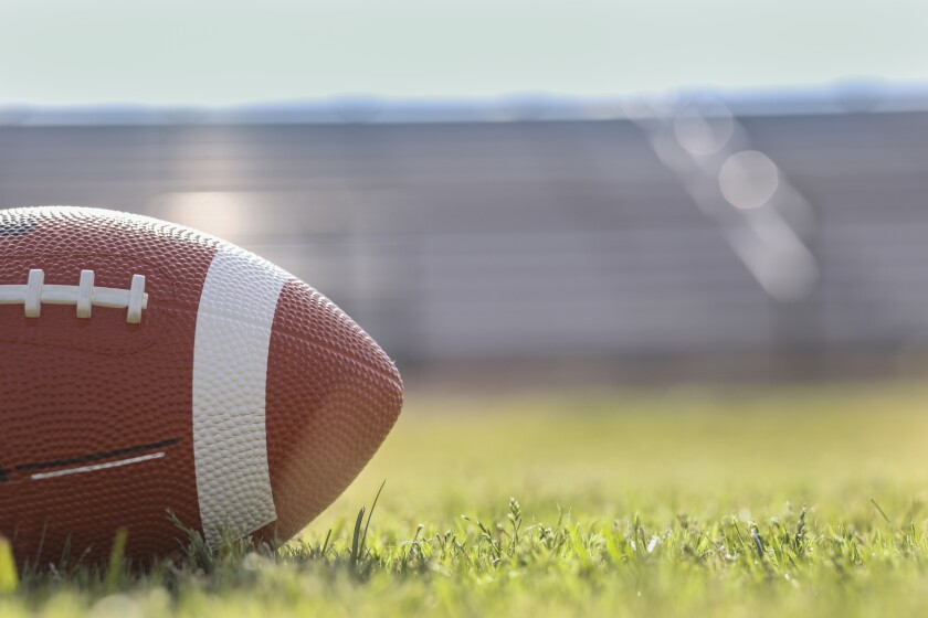 Football on grass stadium on college or high school campus. Bleachers background.