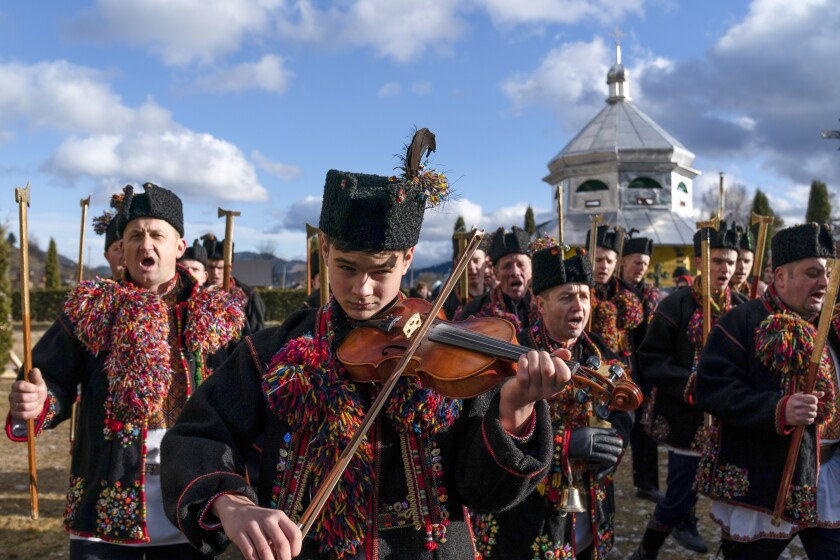 An ethnic Hutsul man, an ethnic group spanning parts of western Ukraine, plays a violin as others, all wearing traditional colorful clothes, sing a kolyada song during the Orthodox Christmas celebration near the Holy Trinity church in Iltsi village, Ivano-Frankivsk region of Western Ukraine, Thursday, Jan. 7, 2021. Orthodox Christians celebrate Christmas on Jan. 7, in accordance with the Julian calendar. (AP Photo/Evgeniy Maloletka)