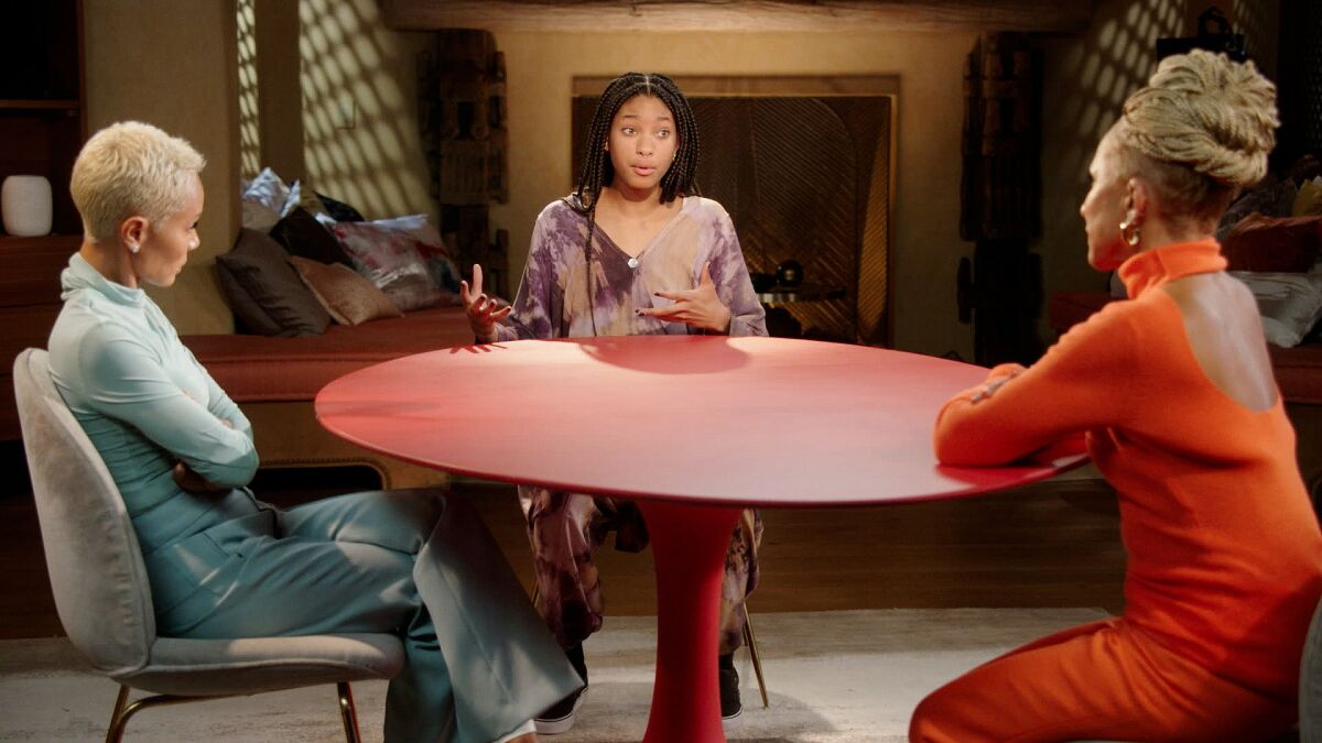 One woman talking to two older women sitting at a red table