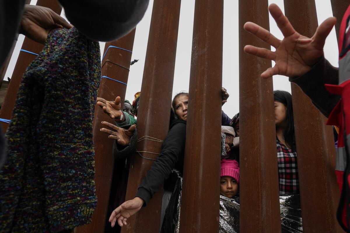 People reach through slats in a border wall as volunteers hand out clothing.