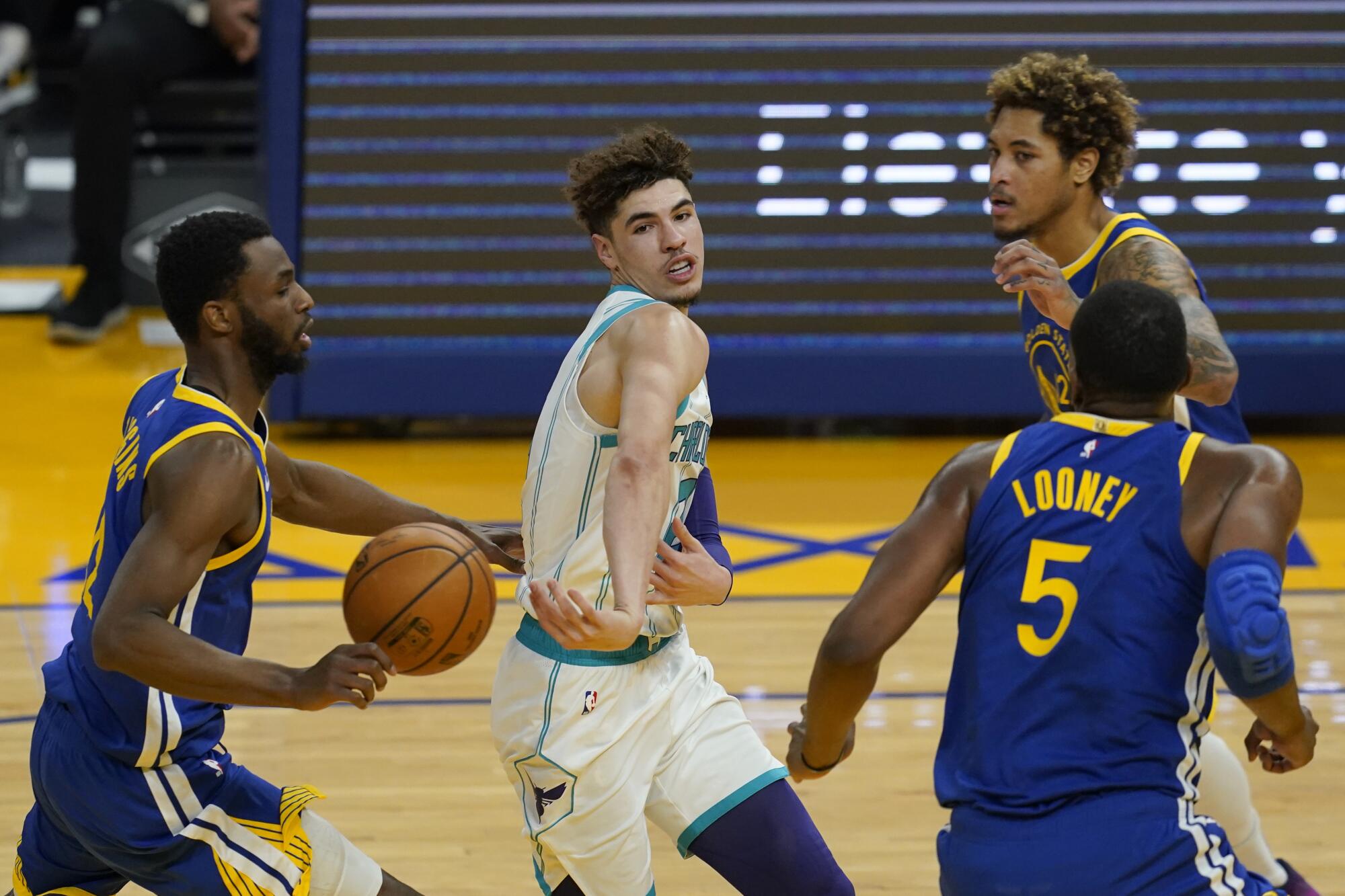 Hornets guard LaMelo Ball flips a pass while surrounded by Warriors defenders.