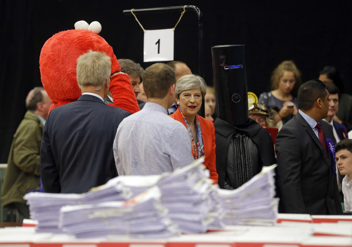 Prime Minister Theresa May, center, stands between candidates Elmo and Lord Buckethead as she awaits the election results in Maidenhead, England. (Alastair Grant / Associated Press)