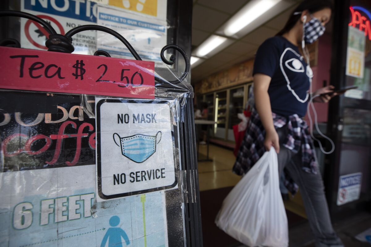 A woman leaves a market in Chinatown where a sign at the entrance says, "No mask no service."