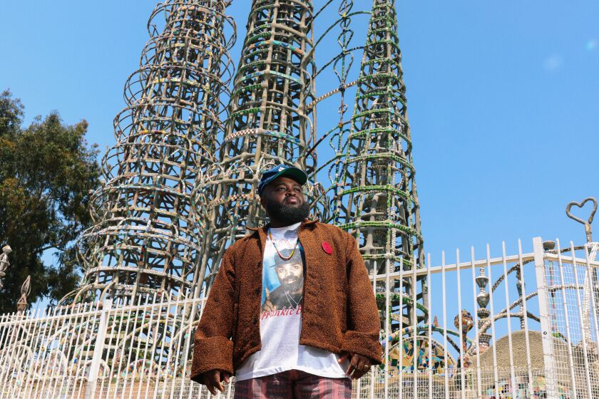 A man stands in front of the Watts Towers.