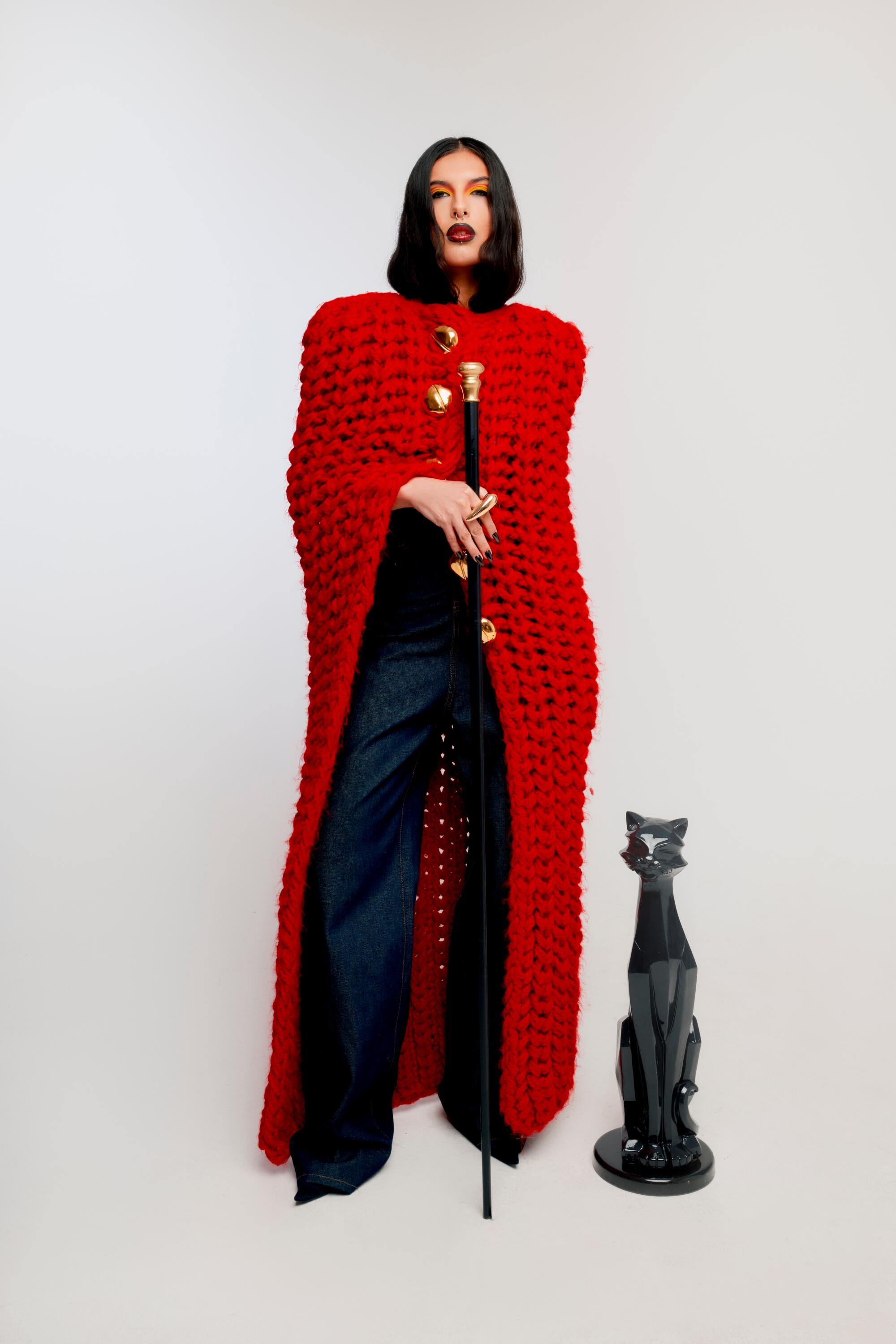A woman wears a red knit sweater and stand beside a sculpture of a black cat.