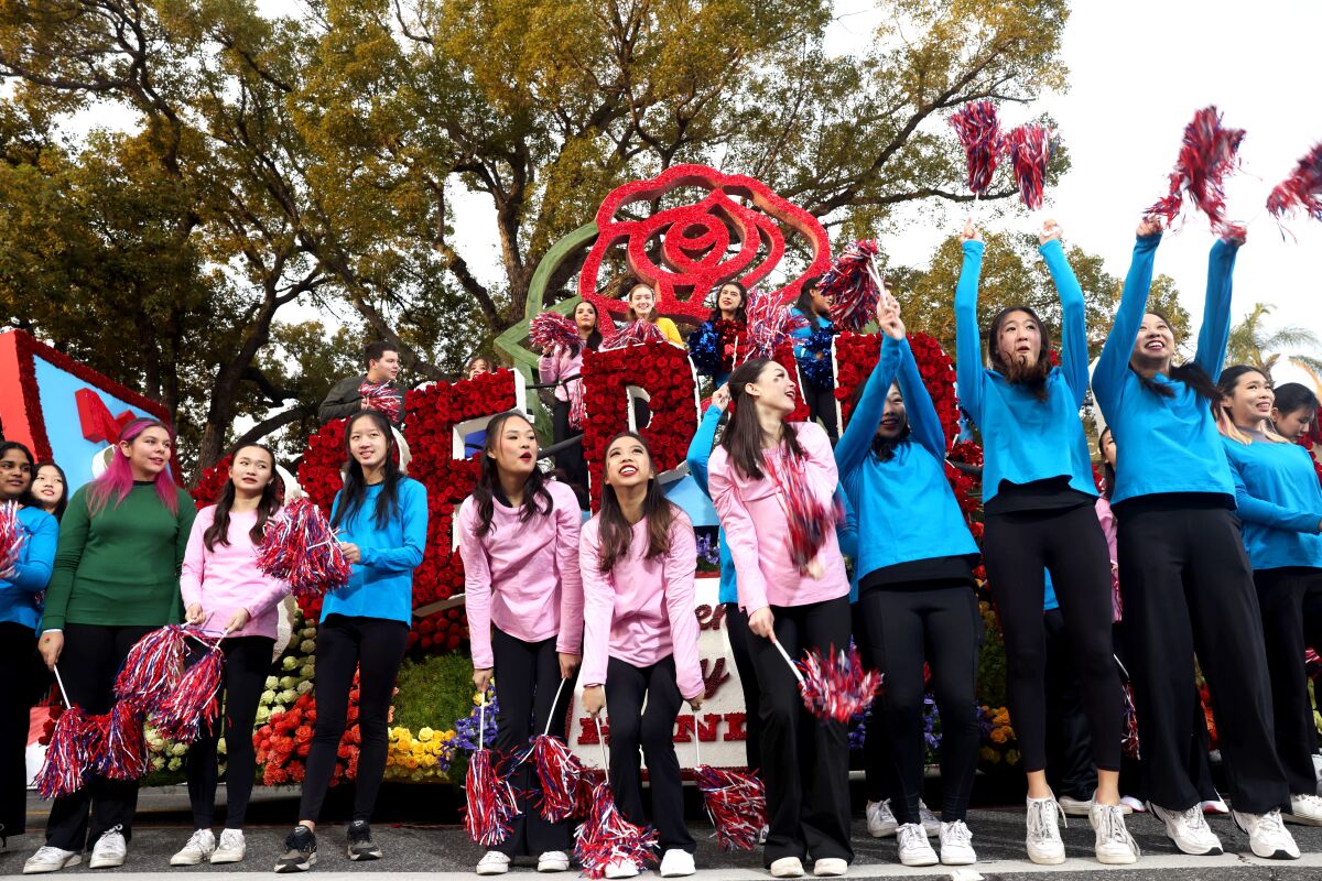 Performers in pink, blue and green shirts wave pom-poms at the Rose Parade.