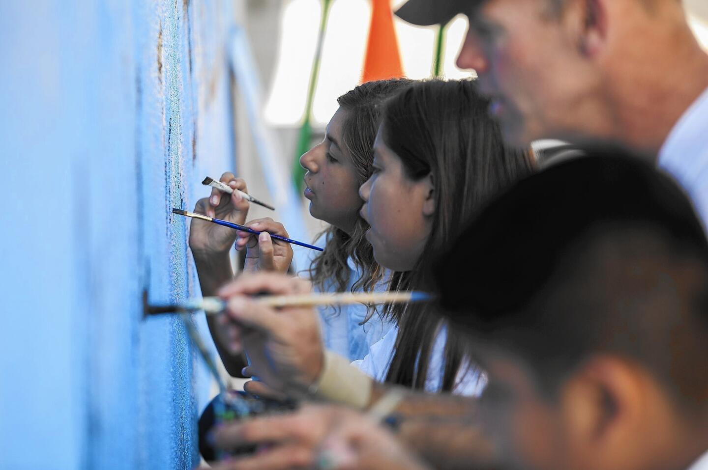 Michael Howard, founder of Operation Clean Slate, a mural-making organization, paints a mural with Rea Elementary school students Ricardo Contreras, 11, left, Xamantha Rocha, 11 and Alicia Airey, 10 on a wall at school on Tuesday.