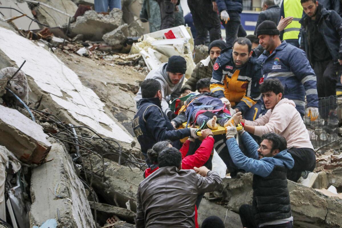 A person on a stretcher is handed down a mountain of rubble by rescuers after being pulled from a collapsed building