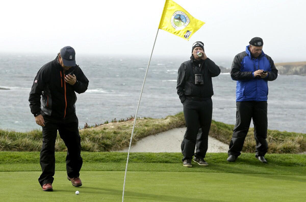 A PGA Tour official, left, watches to see if a ball moves in the wind on the fourth green of the Pebble Beach Golf Links. Play was suspended for more than 2 hours because of high winds.