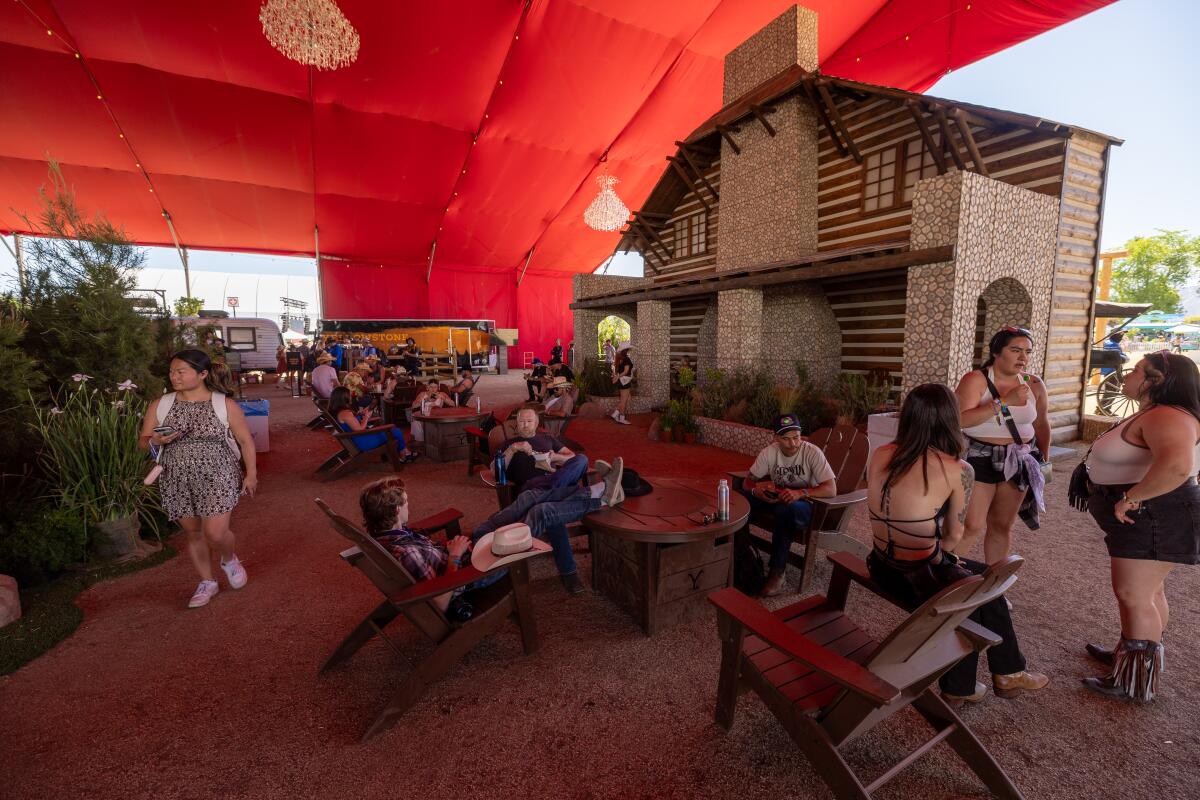 People sit in rustic chairs in a red tent with a lodge facade in the background