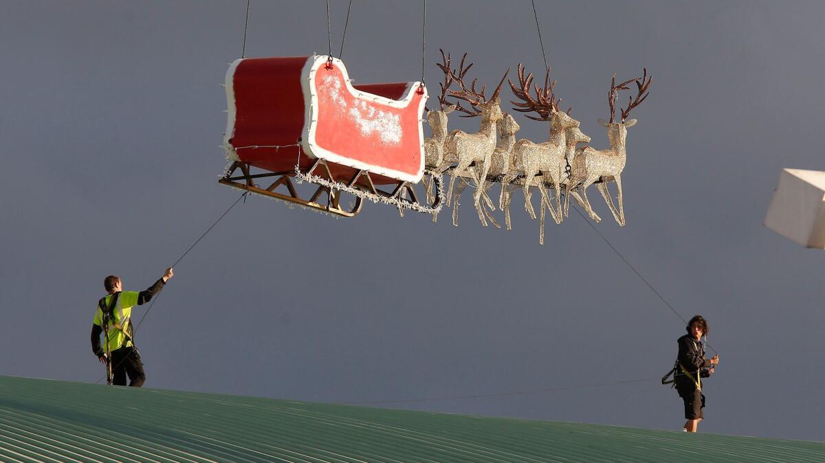 Santa's sleigh and reindeer, guided into position from a crane by two workers, near their destination on the roof of the Hangar at the OC Fair & Events Center for Winter Fest on Thursday.