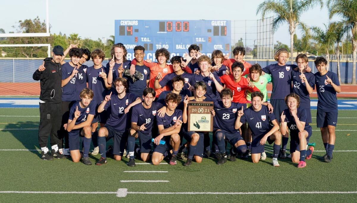 Players gather on a soccer field for a team picture. One player holds a large plaque.