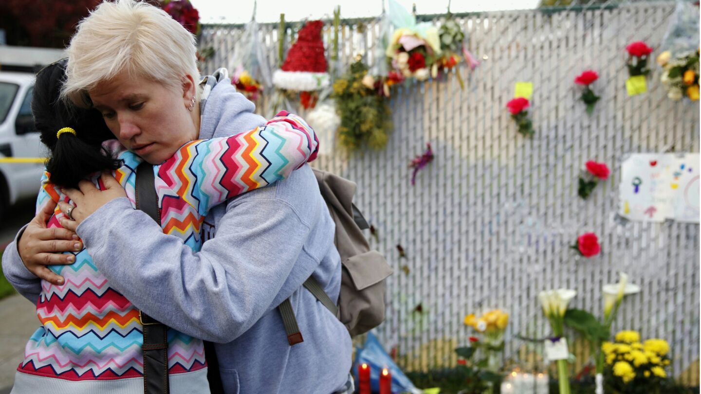 Kristen Grzeca, a music teacher at Ruth Asawa San Francisco School of the Arts, hugs Monina Sen Cervone, director of world music and dance at the school, on Sunday at a makeshift memorial for victims of the warehouse fire. A 17-year-old victim was one of Grzeca's students.