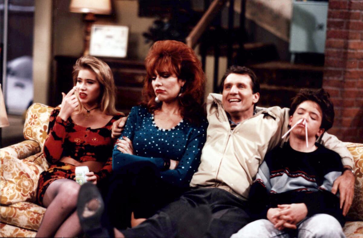 Kelly, Peggy, Al and Bud Bundy sit on a yellow couch in their living room.