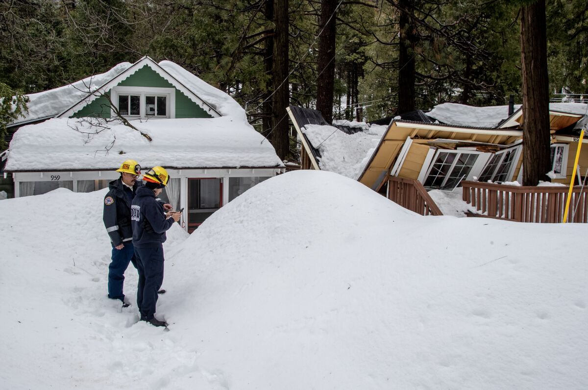 Two people in yellow hard hats look at a broken roof in a snowy landscape.