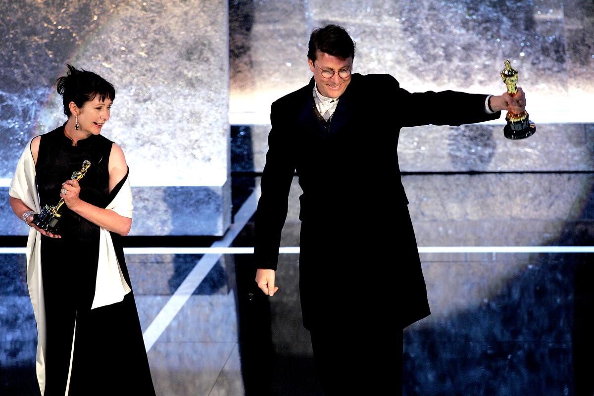 A man and woman stand on stage holding Oscars.