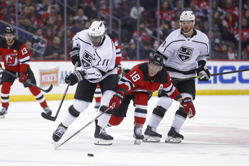 New Jersey Devils forward Ondrej Palat (18) tries to reach the puck from between Los Angeles Kings forward Anze Kopitar, left, and forward Adrian Kempe during the second period of an NHL hockey game Thursday, Feb. 15, 2024, in Newark, N.J. (AP Photo/John Munson)