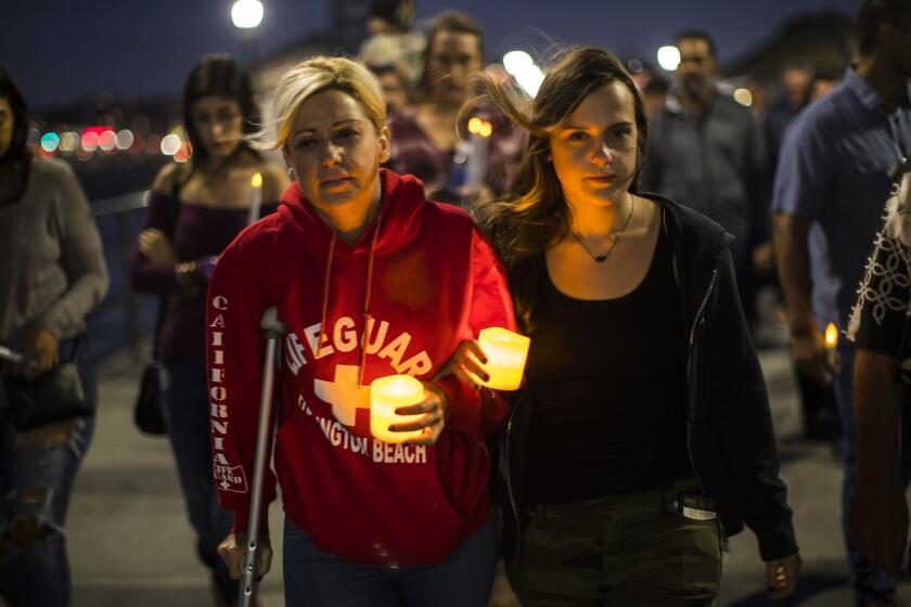 Walking with a crutch, shooting victim Tiffany Katsaris,45, of Huntington Beach, left, walks arm-in-arm with her daughter Tara Handshaw, right, during a candlelight procession on the Huntington Beach Pier.