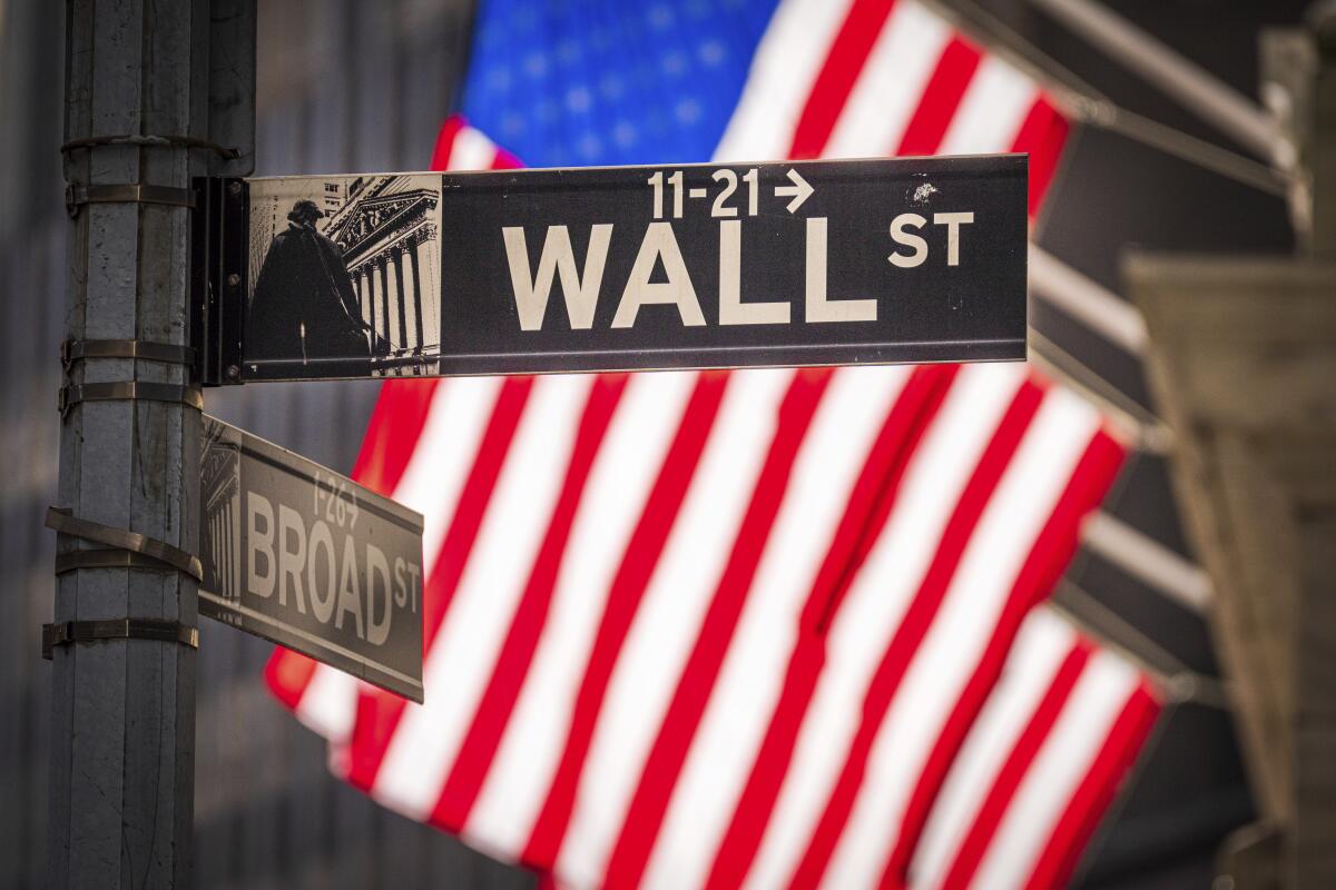 U.S. flags hang from a building that is behind a Wall Street sign.