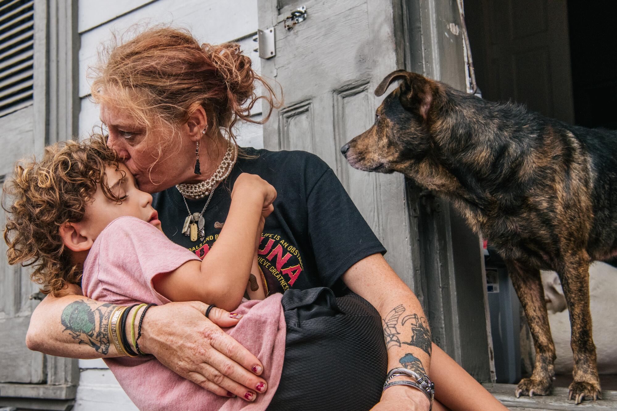 A woman holds a young boy next to a dog.