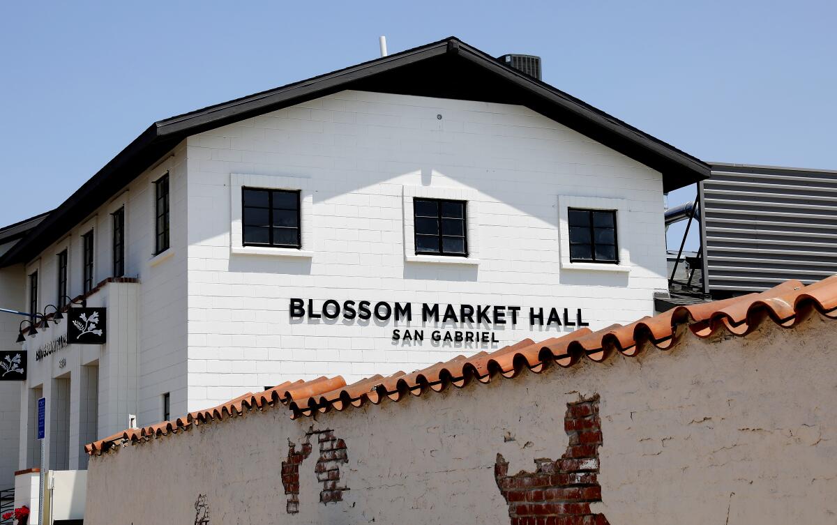 A photo of the exterior of a large white building with a sign that says "Blossom Market Hall San Gabriel"
