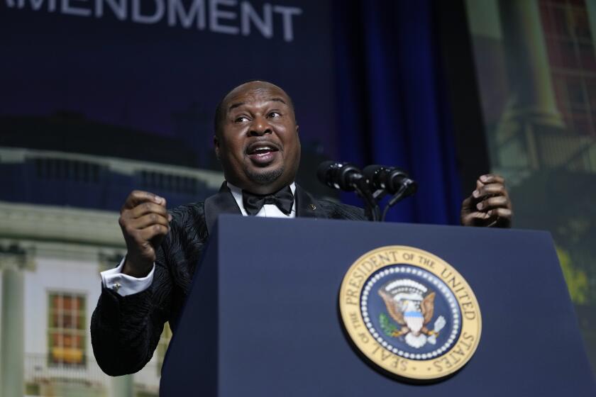 Roy Wood Jr. speaks into a microphone and gestures behind a presidential lectern